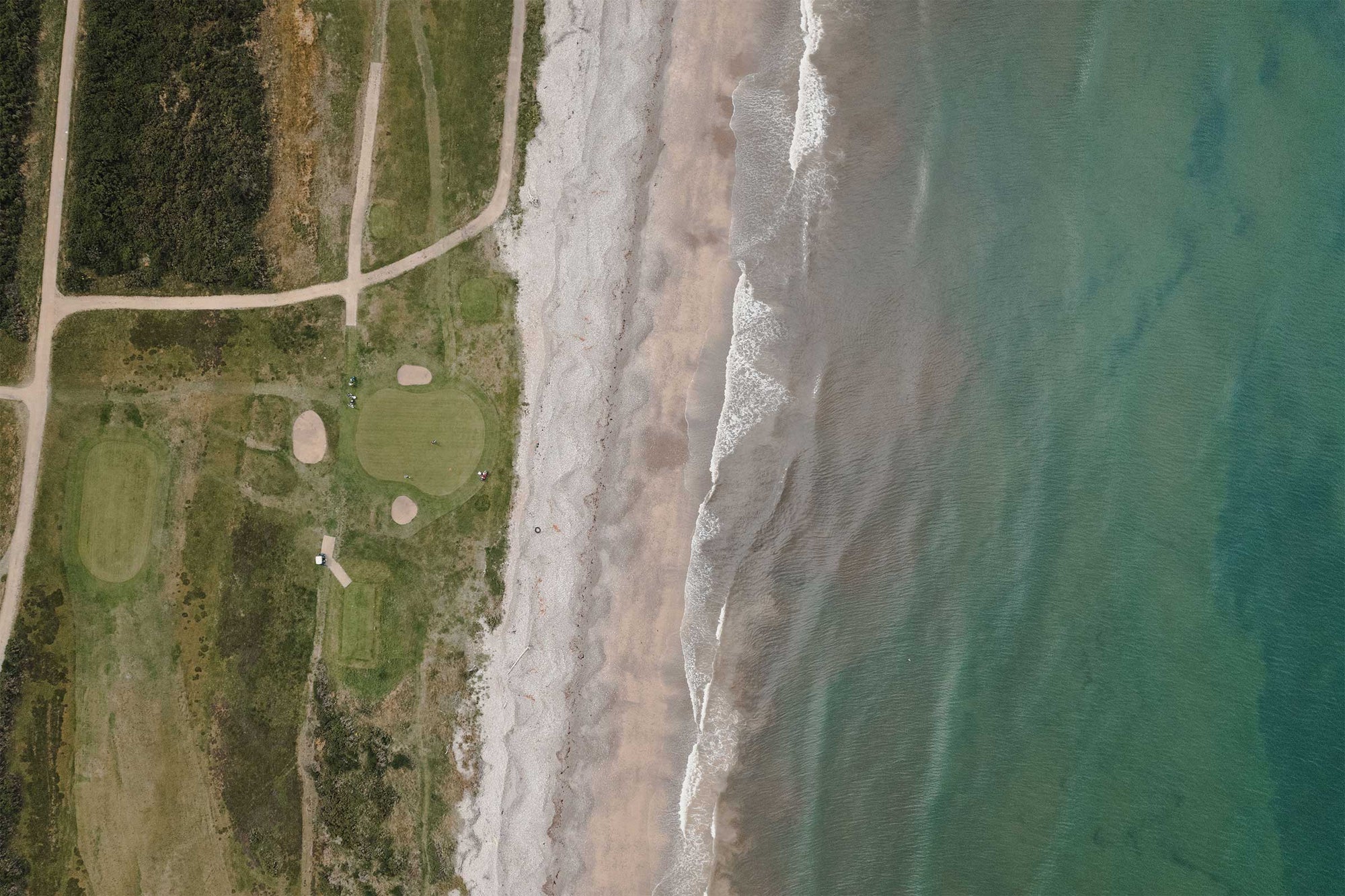 Overhead hero image of Spey Bay Golf Club: a drone image showing a golf green complex with the sea and waves and beach.